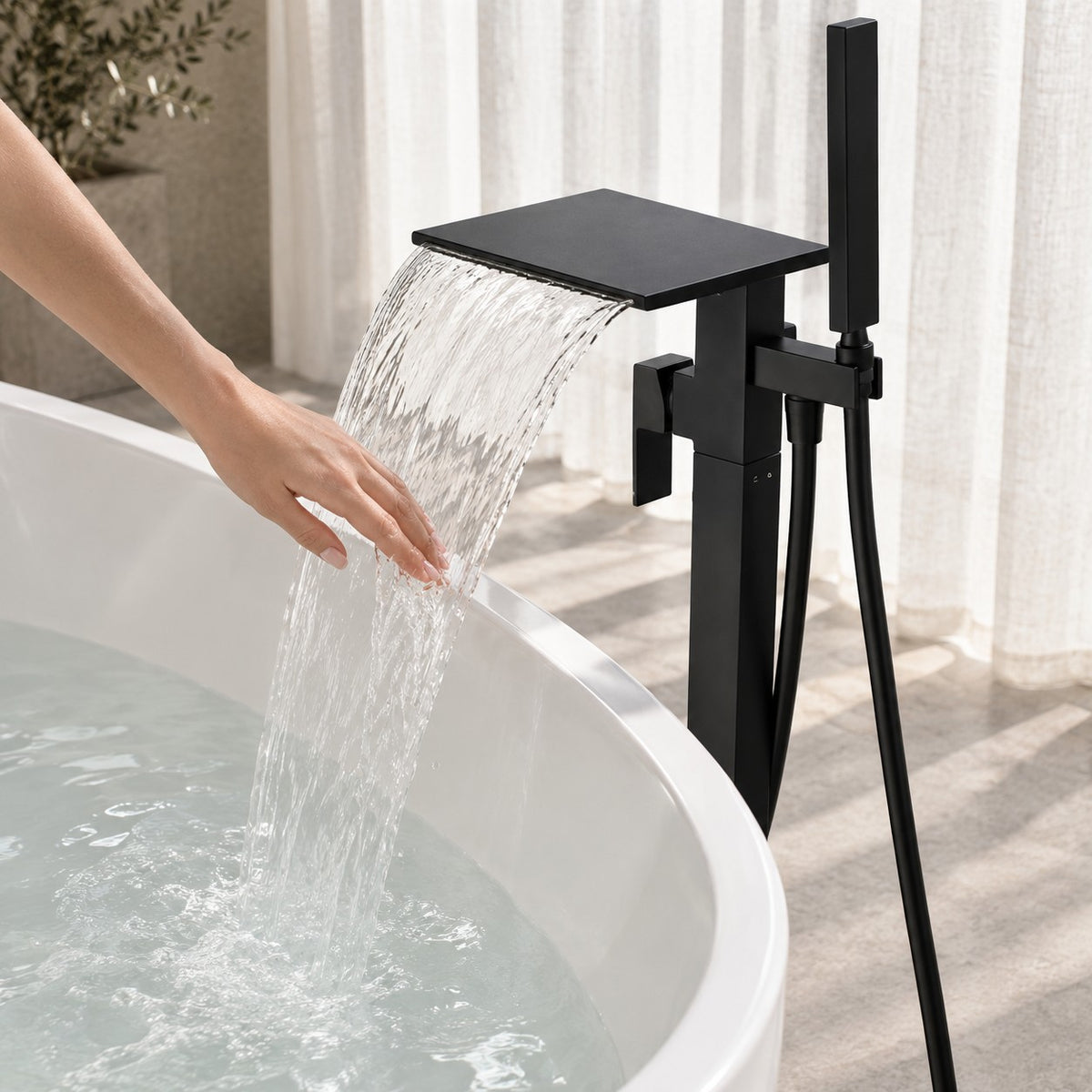 Mitigeur baignoire sur pied cascade MONZARIO avec une main sous le jet, baignoire îlot, mise en situation
