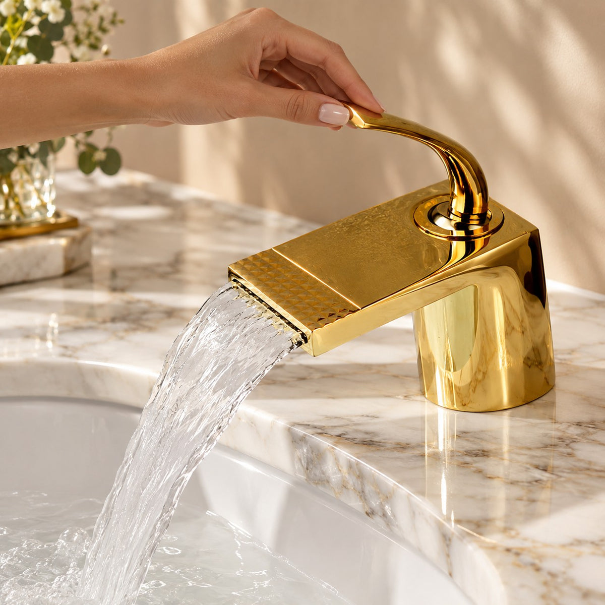 Mitigeur lavabo cascade doré AURELIO avec une main sur la commande, plan en marbre, mise en situation