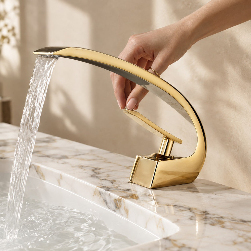 Mitigeur lavabo design courbé LUNAVIO doré avec une main près de la manette, plan en marbre, mise en situation