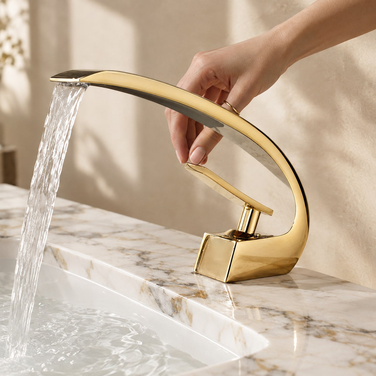 Mitigeur lavabo design courbé LUNAVIO doré avec une main près de la manette, plan en marbre, mise en situation